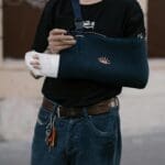 A man wearing a dark sling with a bandaged arm, standing outdoors in casual attire.